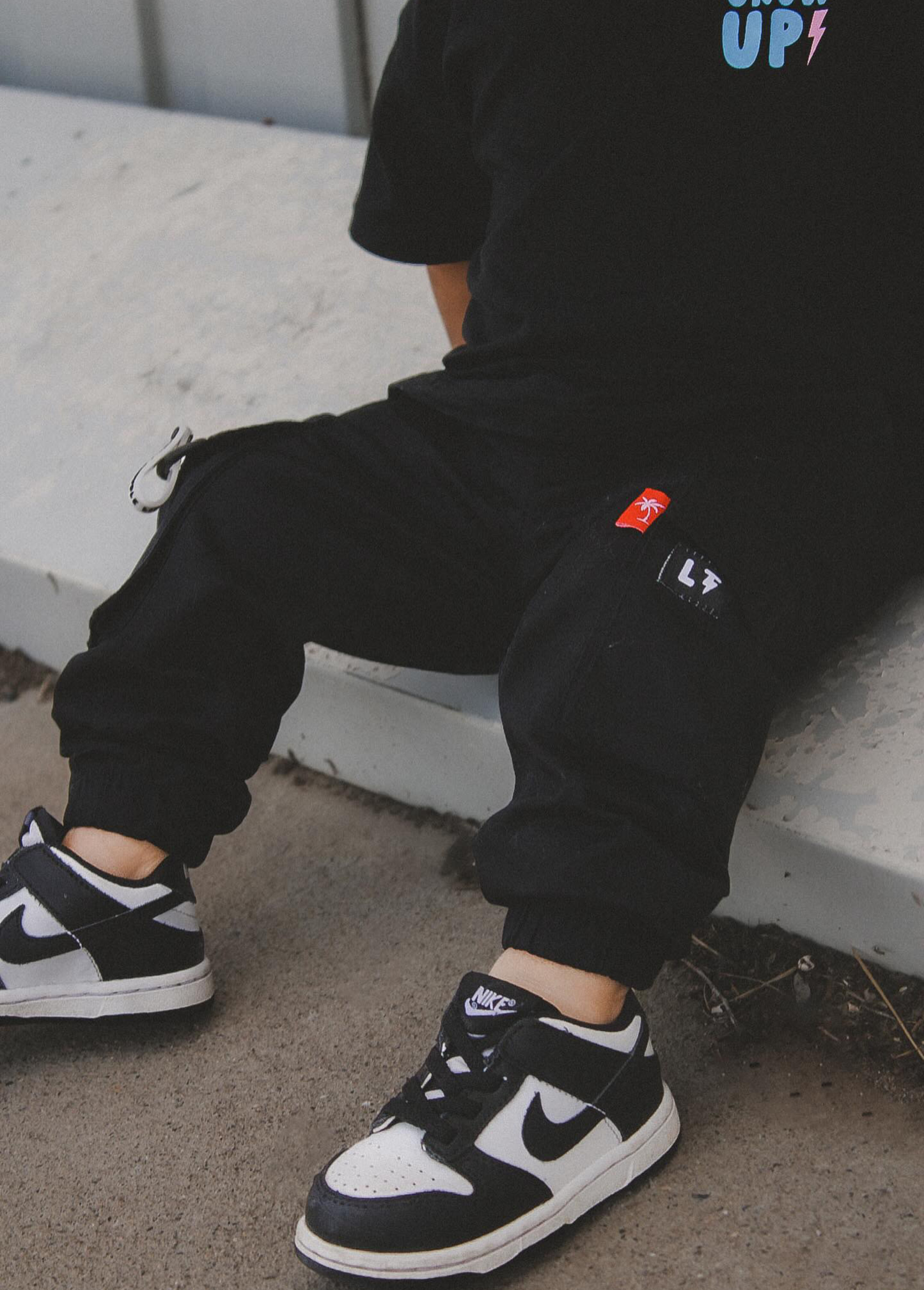 Kids unisex black cargo pants with ankle cuffs and clip label details flat lay view