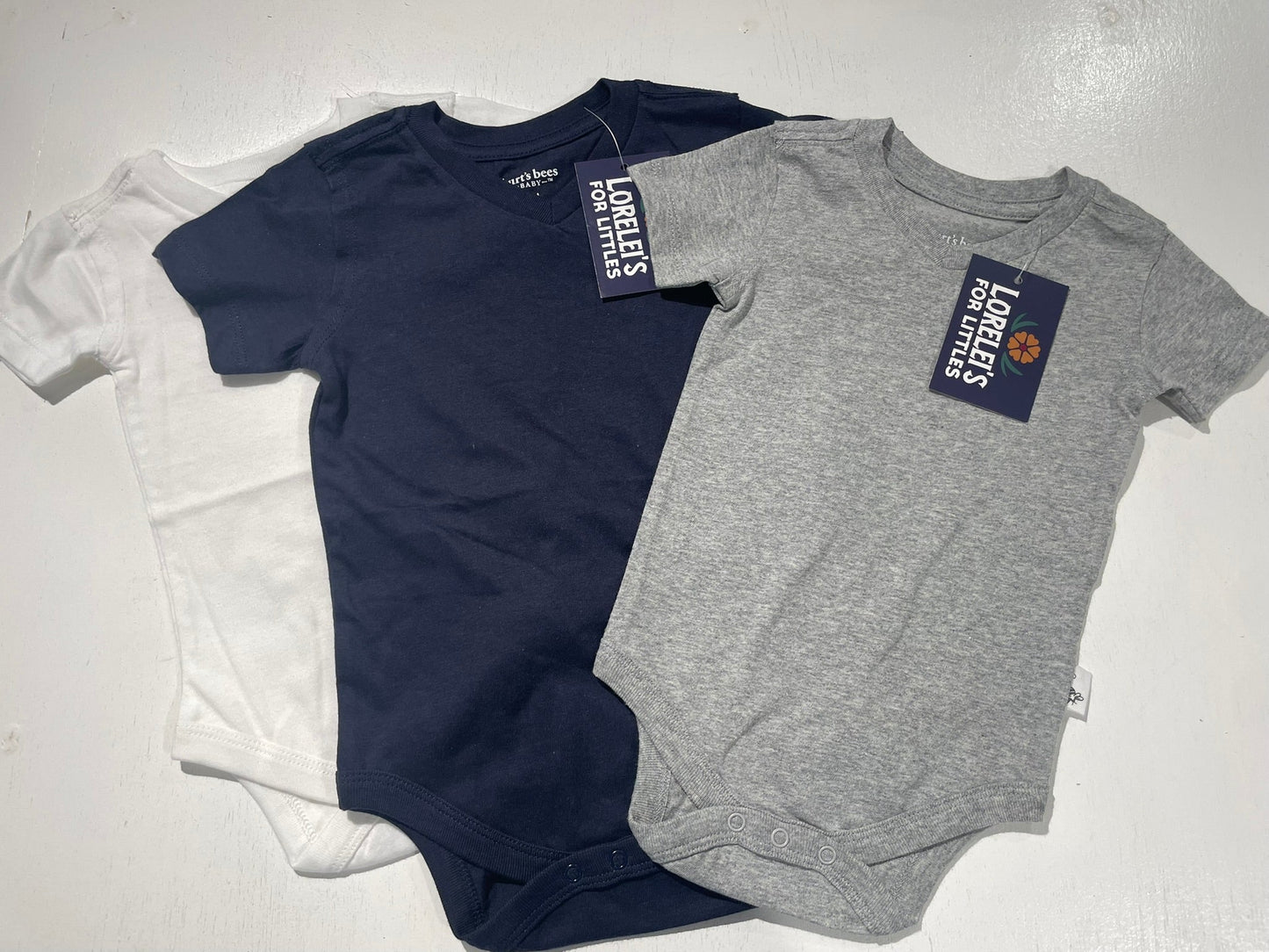 Two baby onesies, one navy and one gray, with labels on a white background.