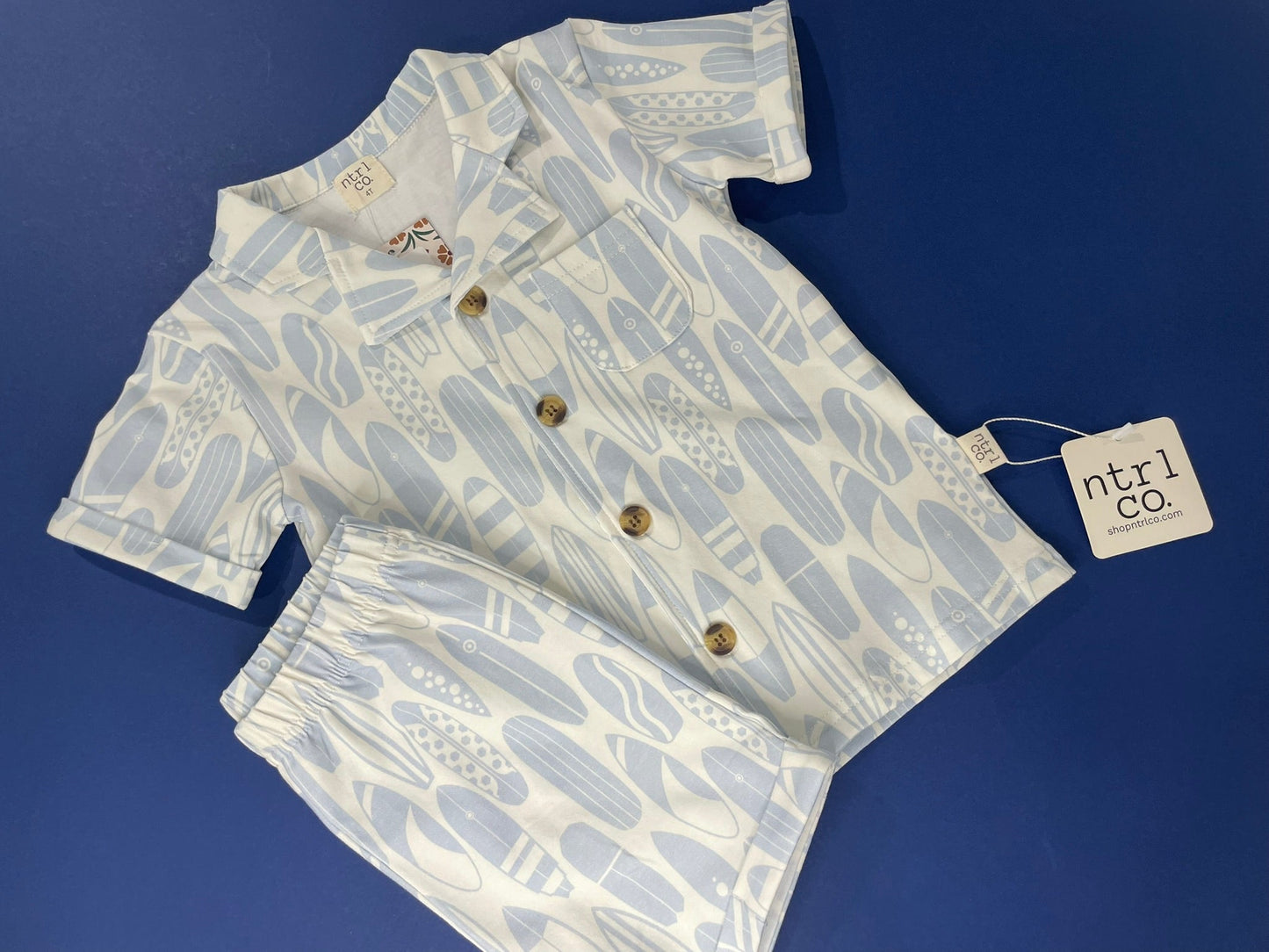 Children's outfit with shirt and shorts on a blue background, featuring a pattern of fruits and vegetables.