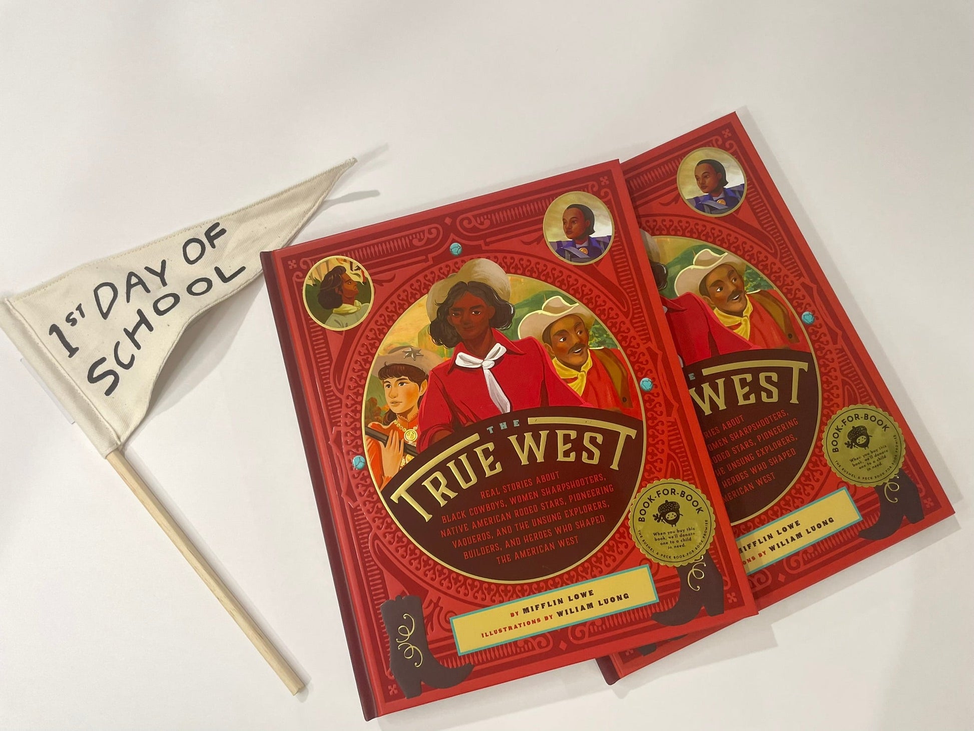 Red book titled 'True West' with a '1st Day of School' flag on a white background